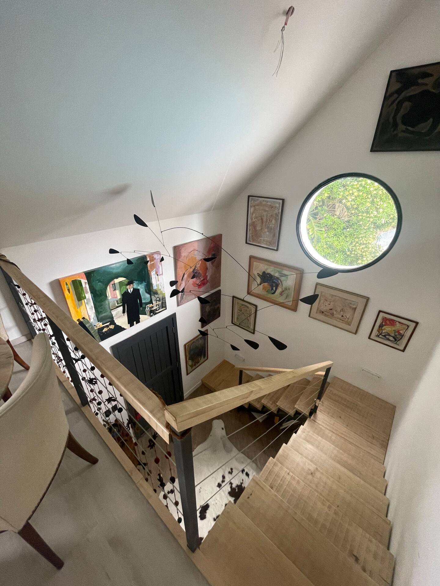 Staircase with gallery wall of art, mobile sculpture and round window